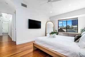 A modern bedroom with a bed, a flat-screen TV, a large mirror, and a window with a view of buildings. - Palm Beach Oasis a comfortable three-bedroom townhouse (Palm Beach)