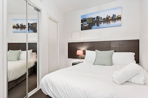 Ein Hotelzimmer mit einem großen Bett, einem Nachttisch, einer Lampe und einem Stadtbild an der Wand.