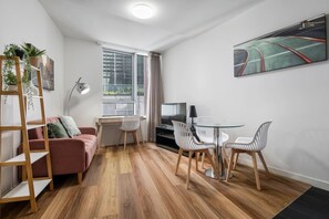 Ein modernes Wohnzimmer mit einer Couch, einem Fernseher, einem Glastisch mit Stühlen, einer Holzleiter und einem Bild an der Wand.