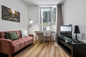 A modern living room with a pink sofa, a desk, a chair, a TV, and a lamp. - Central Studio by QV Market (Carlton South)