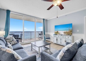 A living room with a sofa, a coffee table, and a television. There is a balcony with a view of the ocean. - Majestic Memories 1302-Gulf Front-Sleeps 13 (Panama City Beach)