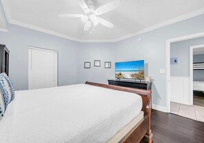 A bedroom with a bed, a ceiling fan, a television, and a door leading to another room. - Majestic Memories 1302-Gulf Front-Sleeps 13 (Panama City Beach)