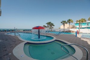 A pool area with a water feature, lounge chairs, and a view of the ocean. - Majestic Memories 1302-Gulf Front-Sleeps 13 (Panama City Beach)