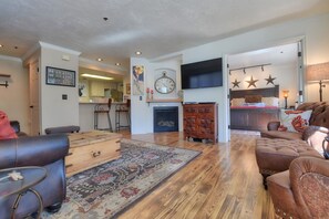A spacious living room with a fireplace, a television mounted above it, and a dining area with bar stools. - Slopeside on Empire: Walk to Park City Mountain Lifts & Main Street | Free Bus (Park City)