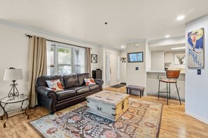 A living room with a leather sofa, a coffee table, a patterned rug, a television, and a kitchen area with a chair. - Slopeside on Empire: Walk to Park City Mountain Lifts & Main Street | Free Bus (Park City)