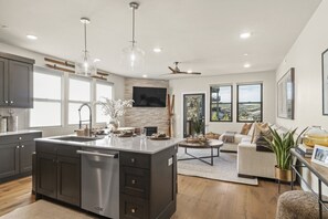 A modern kitchen with a large island, dark cabinetry, and a stone backsplash. - Newly Renovated! 3-Bed with Free Shuttle, Free Ski Waxes + Grill (Daniel)
