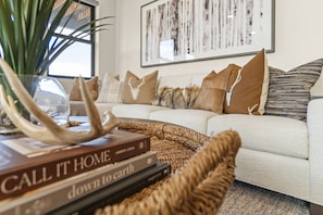 A living room with a sofa, decorative pillows, a woven coffee table, and books. - Newly Renovated! 3-Bed with Free Shuttle, Free Ski Waxes + Grill (Daniel)