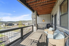 A covered outdoor seating area with a table and chairs, a stone fireplace, and a view of a residential neighborhood. - Newly Renovated! 3-Bed with Free Shuttle, Free Ski Waxes + Grill (Daniel)