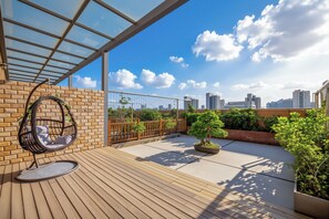 A rooftop terrace with a hanging chair, potted plants, and a city skyline view. - AMBER CRYSTALINTERNATIONAL HOTEL (Shenzhen)