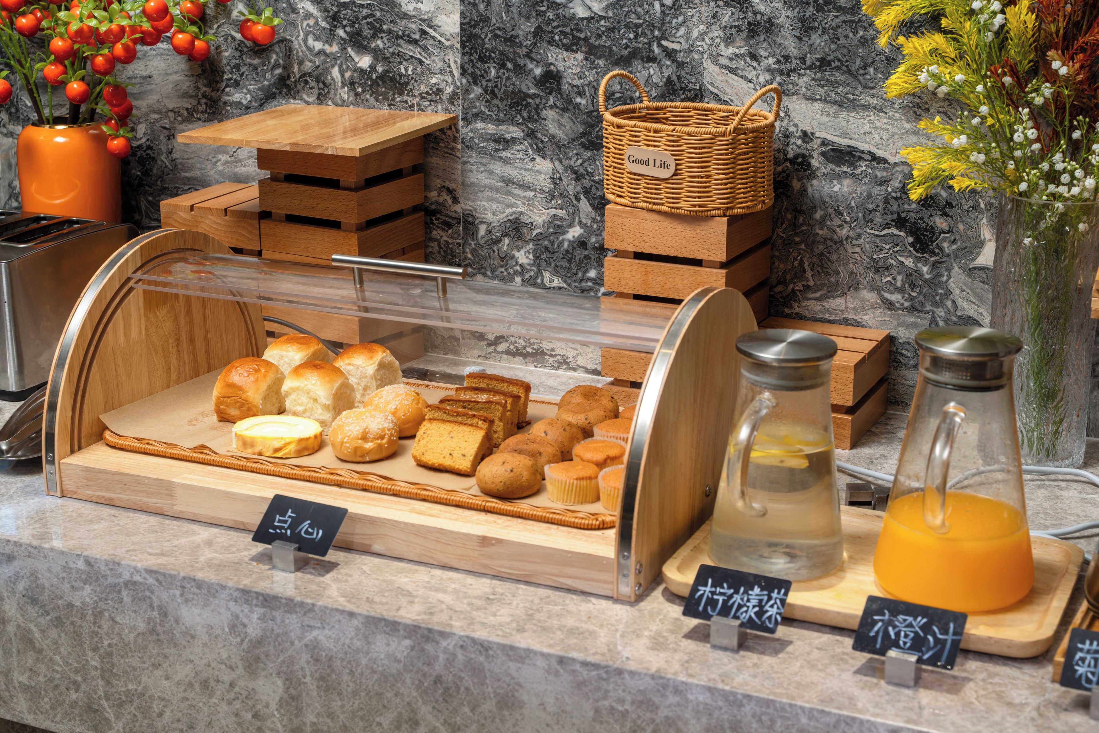 A bakery display with various baked goods and two glass bottles with orange liquid.