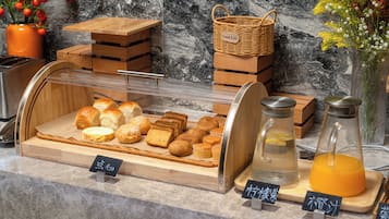 A bakery display with various baked goods and two glass bottles with orange liquid.