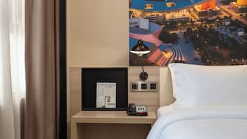 A hotel room with a bed, a nightstand with a lamp, a framed picture, and a wall-mounted phone.