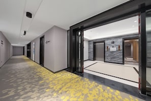 A modern hallway with a patterned carpet, a glass door entrance, and a marble wall. - AMBER CRYSTALINTERNATIONAL HOTEL (Shenzhen)