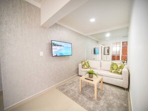 Sala de estar moderna com televisão de tela plana, sofá, mesa de centro e espelho refletindo o ambiente.
