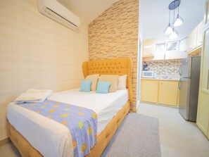 A bedroom with a bed, pillows, a blanket, an air conditioner, a kitchen area with a refrigerator, and a window. - Studio in Sosua Center! Near Sosua beach (Sosúa)