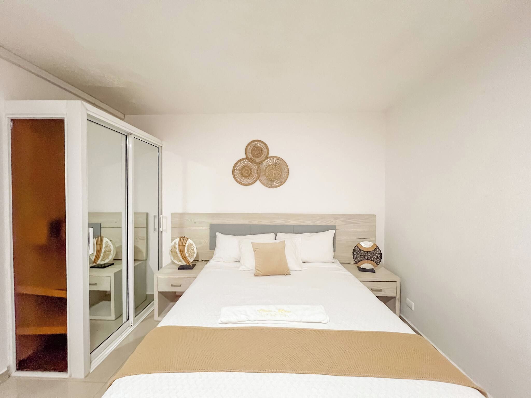 Une chambre d’hôtel comprenant un lit, une table de chevet, une commode, un miroir et une porte coulissante.