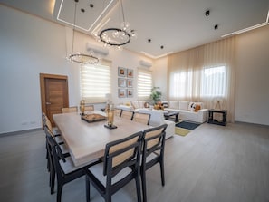 Un salon moderne avec un coin repas, comprenant un lustre, un ensemble de canapés et une table basse.