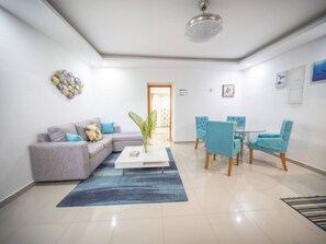 A modern living room with a sectional sofa, a coffee table, a dining area with a table and chairs, and a ceiling fan. - Stylish 1BR Near Beach & Main Strip Sosua (Sosúa)
