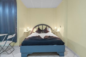 Ein Bett mit Kopfteil, zwei Nachttischlampen und einem zusammenklappbaren Stuhl.