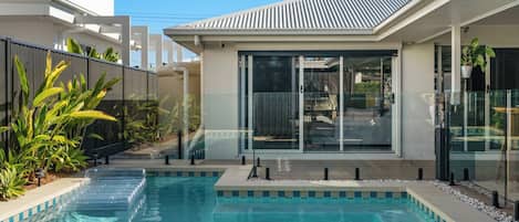 A modern pool area with clear water, surrounded by a glass fence, and adjacent to a building with large windows.