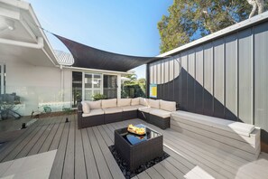 A modern outdoor patio with a sectional sofa, a glass table, and a pool safety sign. - Saltwater Haven - Pool, Beach & Dog-Friendly (Mooloolaba Region)