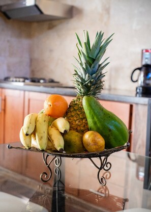 A fruit bowl on a glass table with bananas, pineapple, orange, and a melon. - Getaway room with shared Jacuzzi in the center (Sosúa)
