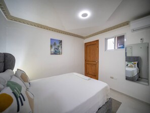 Ein Schlafzimmer mit einem Einzelbett, einer Holztür, einem kleinen Fenster und einem an der Wand befestigten Spiegel.