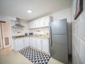 A compact kitchen with white cabinets, a stainless steel refrigerator, a microwave, and a gas stove. - Cozy & Central 3BR Apt Secure & Comfortable (Sosúa)
