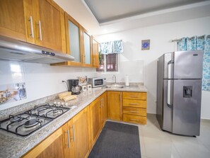 A kitchen with wooden cabinets, a stainless steel refrigerator, a gas stove, and a microwave. - Cozy & Quiet 1BT Apt Central in Sosua (Sosúa)