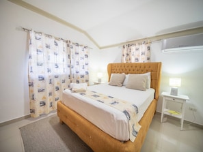 Ein Hotelzimmer mit Bett, Vorhängen, einem Nachttisch mit Lampe und einer Klimaanlage.