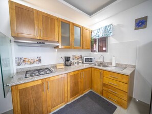 A kitchen with wooden cabinets, a gas stove, a microwave, and a sink. - Cozy & Quiet 1BT Apt Central in Sosua (Sosúa)