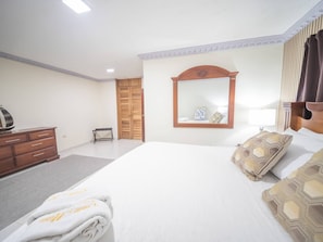 A hotel room with a large bed, a wooden wardrobe, a mirror, and a bedside table. - Spacious 1BR APT in Sosua strip! (Sosúa)