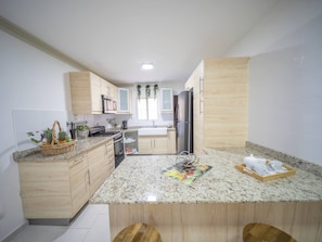 A modern kitchen with granite countertops, wooden cabinets, a central island, and a refrigerator. - Spacious 1BR APT in Sosua strip! (Sosúa)