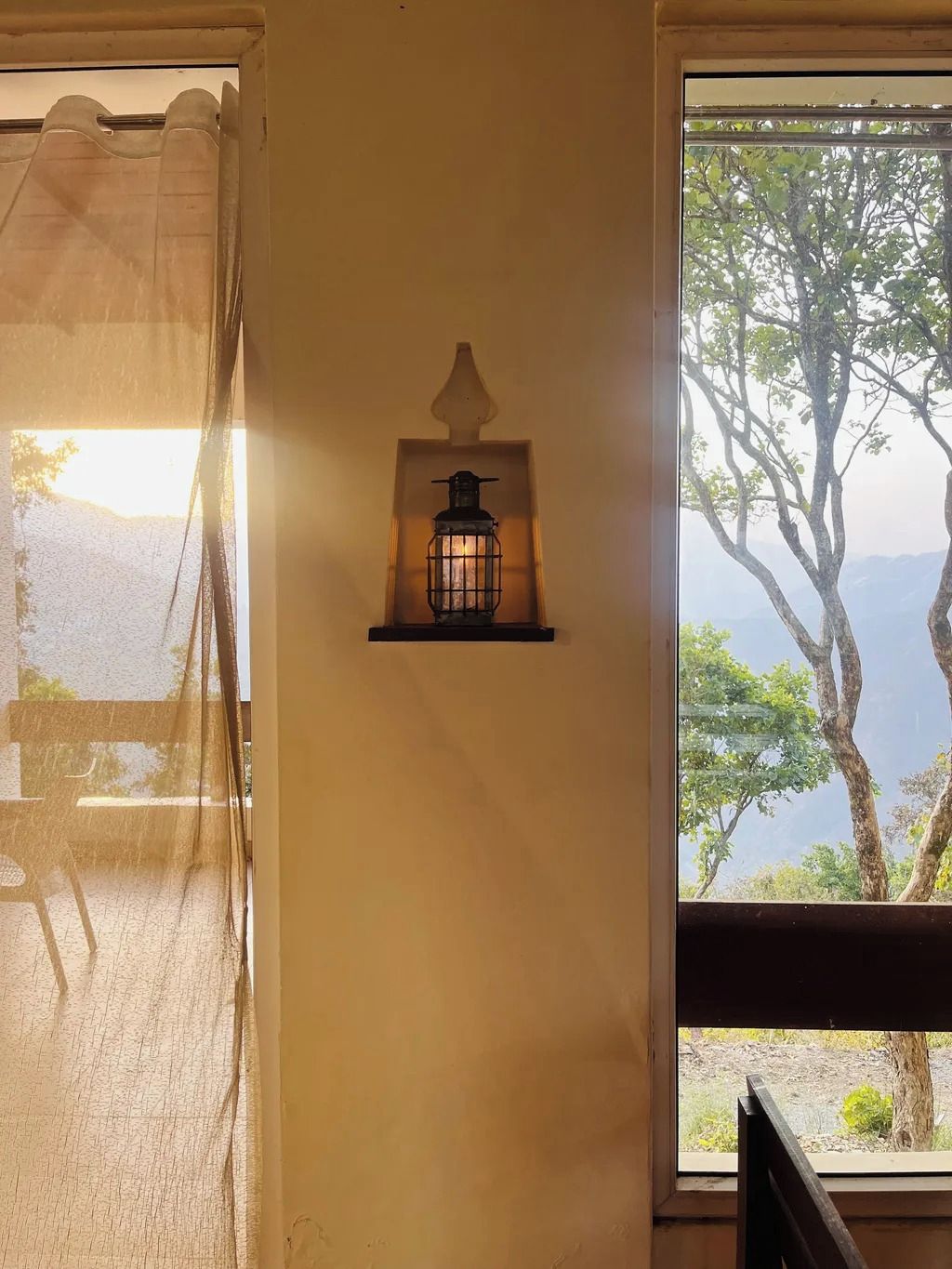 Una lámpara de pared con vistas a árboles y montañas a través de una ventana.