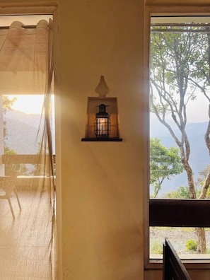 A wall-mounted lantern with a view of trees and mountains through a window. - Auranya The Himalayan Jungle Retreat (Choubattakhal)