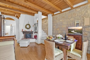 Amplia sala de estar con pared de piedra, techo de madera y una mesa de comedor para dos.