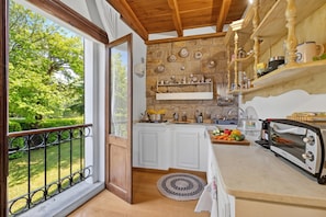 Una cocina con vista a un jardín, armarios de madera, una estufa y diversos utensilios de cocina.