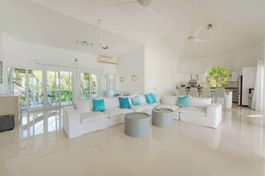 Un vaste espace de vie agrémenté d’un canapé blanc, de deux petites tables rondes et d’une grande fenêtre donnant sur un paysage verdoyant.