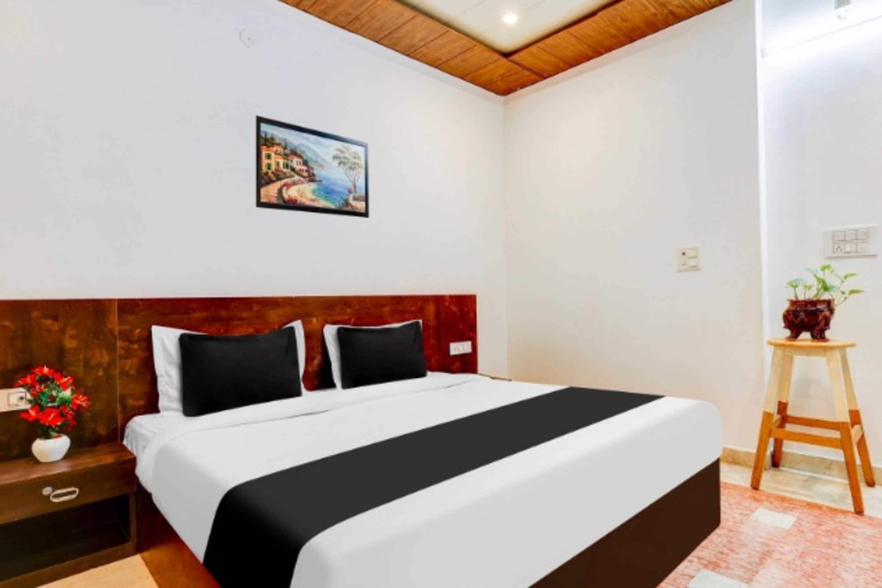 A hotel room with a bed, a nightstand, a small table with a plant, and a painting on the wall.