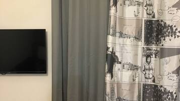 Une salle de bain avec un rideau de douche gris, un téléviseur à écran plat fixé au mur et un radiateur blanc.