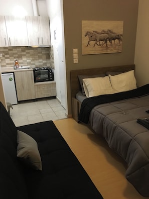 Habitación compacta con kitchenette, una cama con cabecera y un cuadro en la pared.