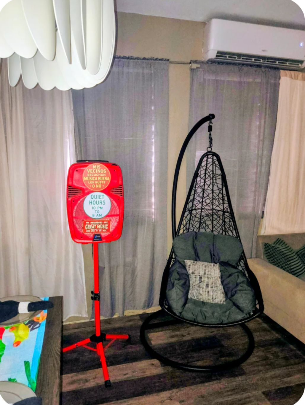 Una habitación con una silla colgante, un altavoz rojo y una ventana con cortinas.