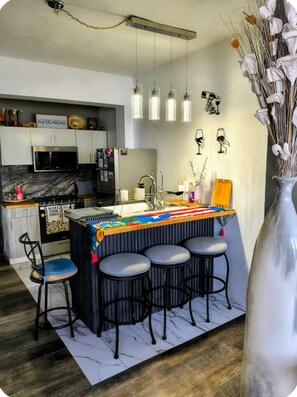 A modern kitchen with a bar area, bar stools, and a decorative vase.