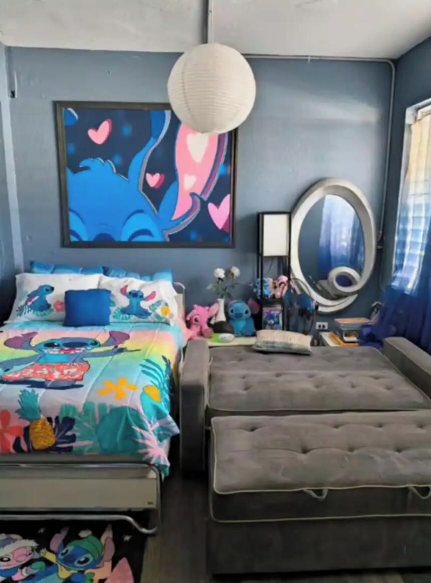 A bedroom with a bed, a tufted ottoman, a wall-mounted mirror, and a framed artwork.