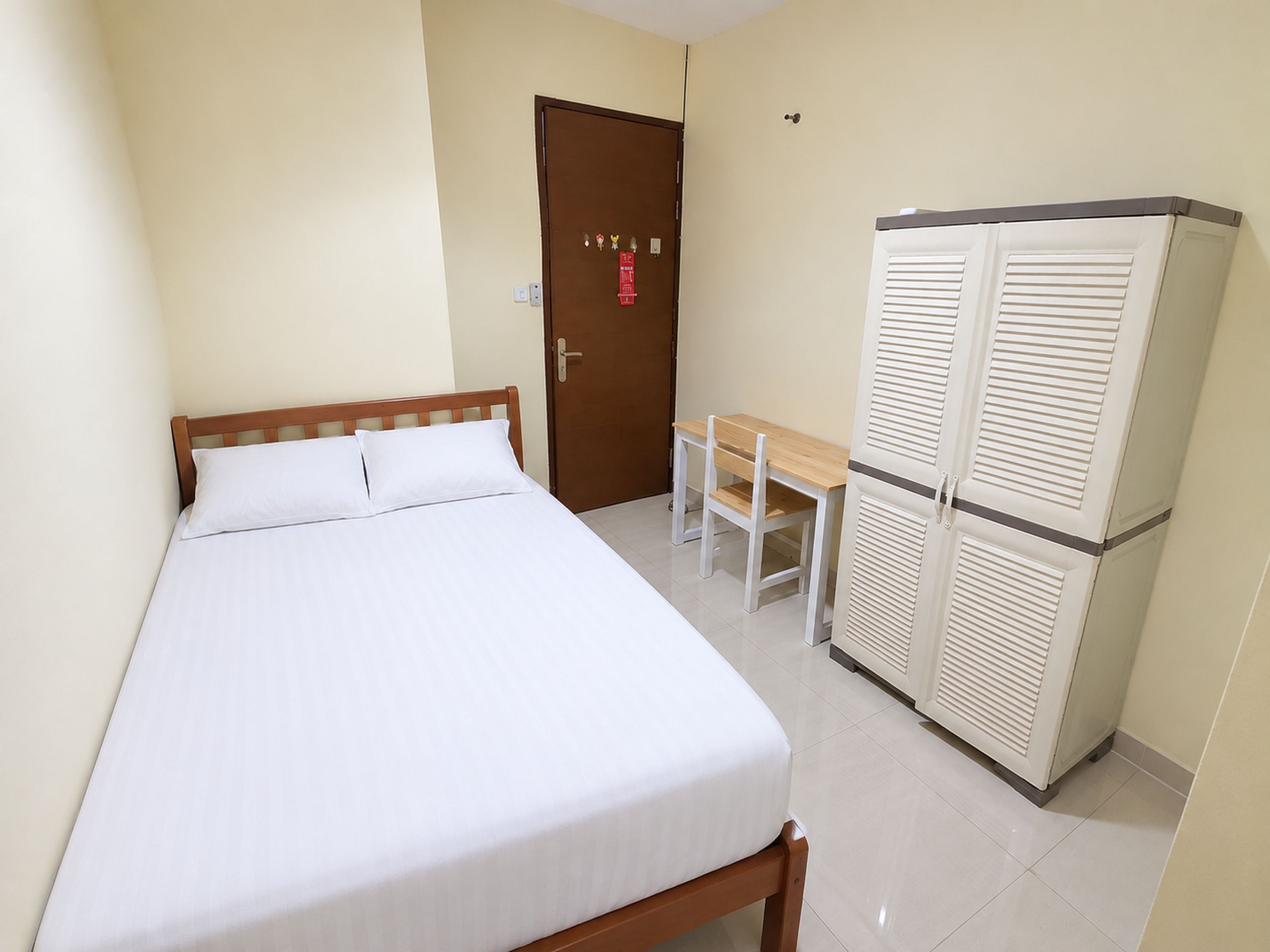 A single bed with a wooden headboard, a small table with two chairs, and a white wardrobe with louvered doors.