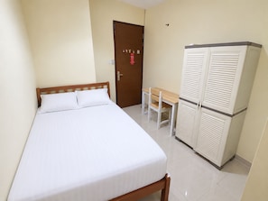 A single bed with a wooden headboard, a small table with two chairs, and a white wardrobe with louvered doors. - Hotel O near Mall Ciputra World  (Jakarta)