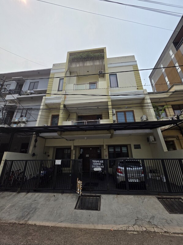 A multi-story residential building with a gated entrance, air conditioning units, and a parked car.