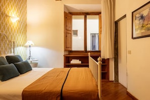 A bedroom with a bed, a nightstand, a lamp, a window with curtains, and a painting on the wall. - The Library by Maison Florence (Florence)