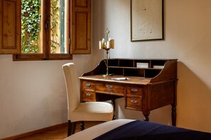 Un bureau en bois avec des tiroirs, une chaise, une lampe et un lit recouvert d’une couverture bleue.