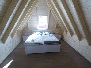A bedroom with a sloped ceiling, a bed, bedside tables, and a window. - Pure sea Breeze (Wurster Nordseeküste)